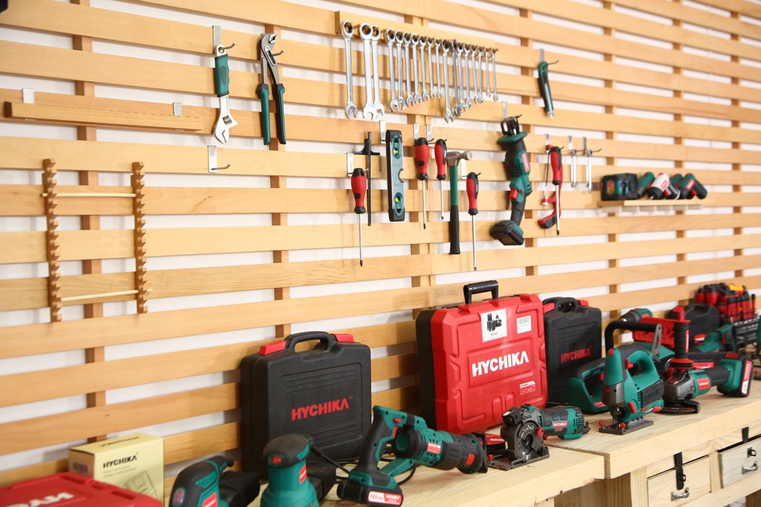 A display of cordless power tools including drills, impact drivers, saws, and sanders arranged on a workshop wall