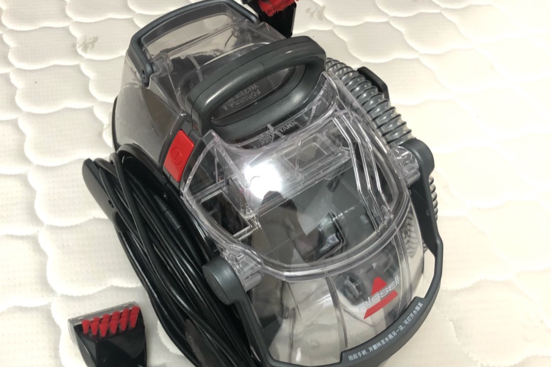 Upright carpet cleaner extracting water from a beige carpet in a residential living room