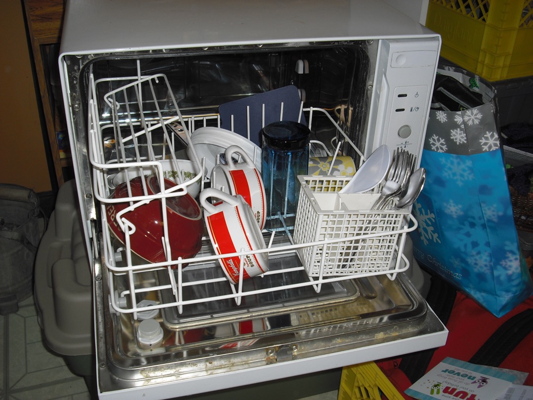 Compact countertop dishwasher sitting on a kitchen counter beside a sink