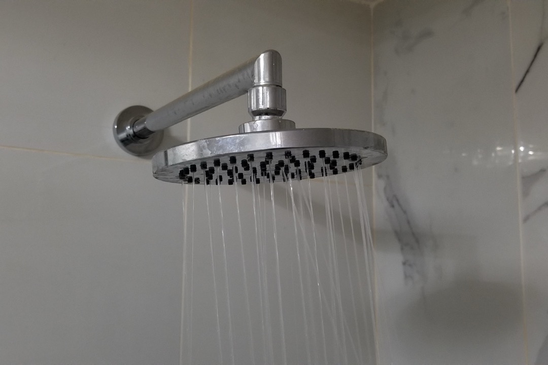 Chrome filtered shower head running in a tiled shower enclosure