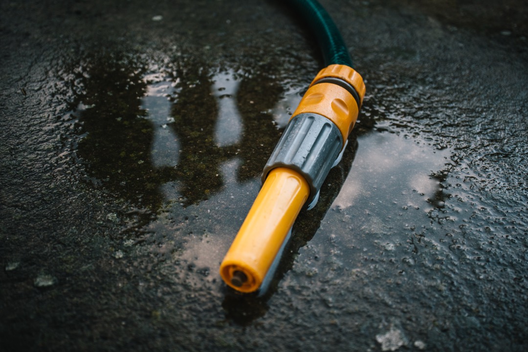Coiled garden hose connected to an outdoor spigot beside a garden bed