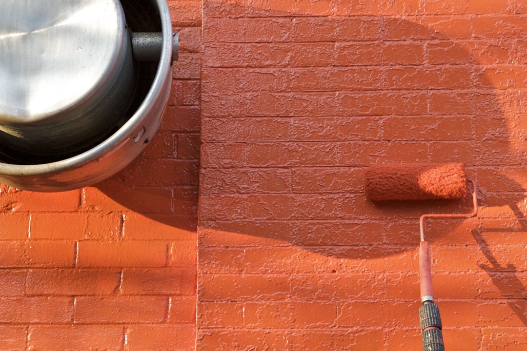 Open gallon of white interior wall paint with a roller and tray on a drop cloth