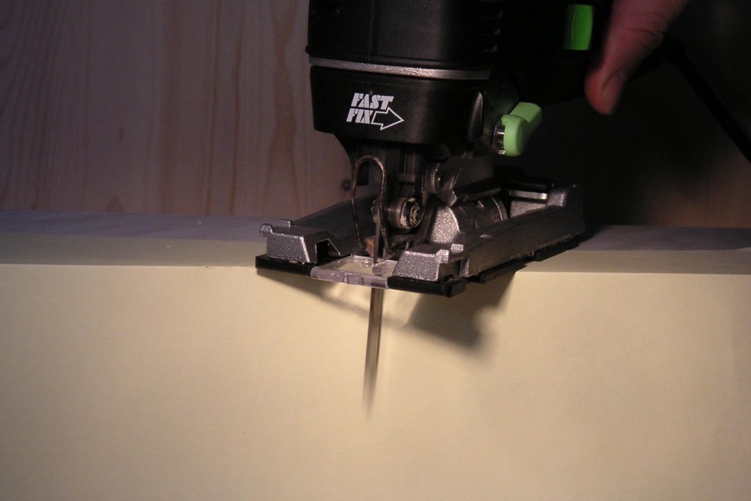 Cordless jigsaw cutting a curved line into a plywood panel on a workbench