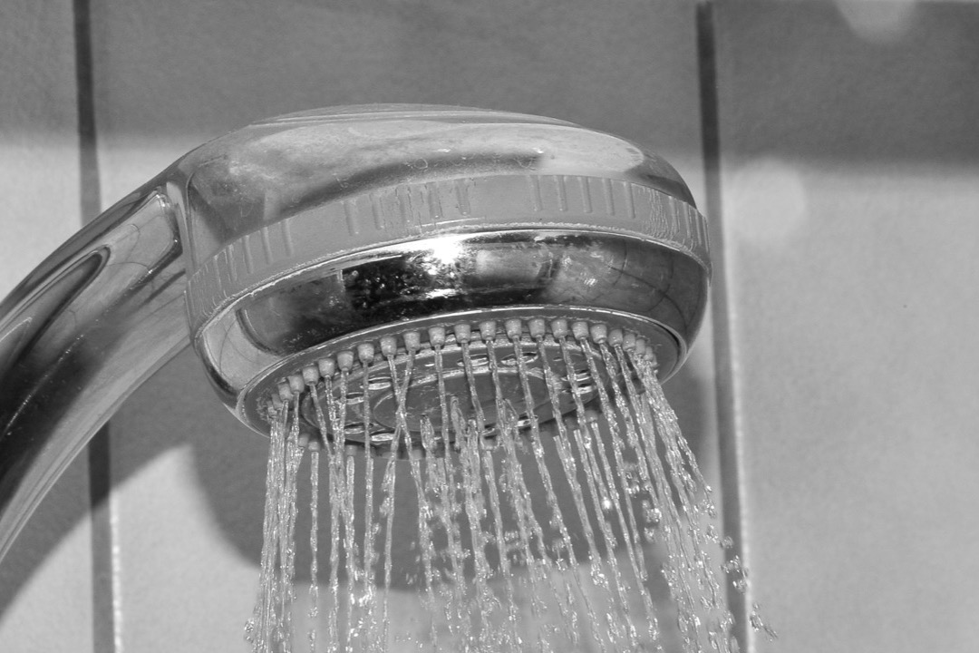 Chrome shower head running with high-pressure spray in a tiled shower