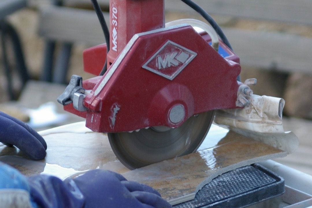Wet tile saw cutting through a porcelain floor tile with water spray