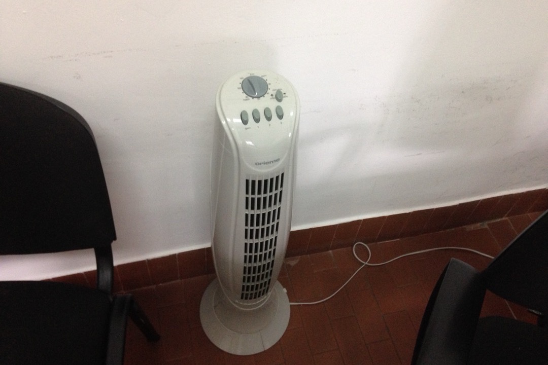 Slim oscillating tower fan standing on a living room floor beside a couch