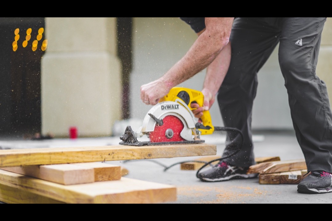 Handheld DeWalt circular saw cutting through a piece of dimensional timber on a workbench