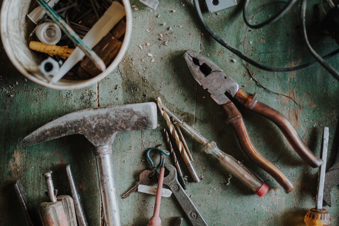 Assorted hand tools arranged on a workbench including a claw hammer, tape measure, screwdriver, pliers, level, and utility knife