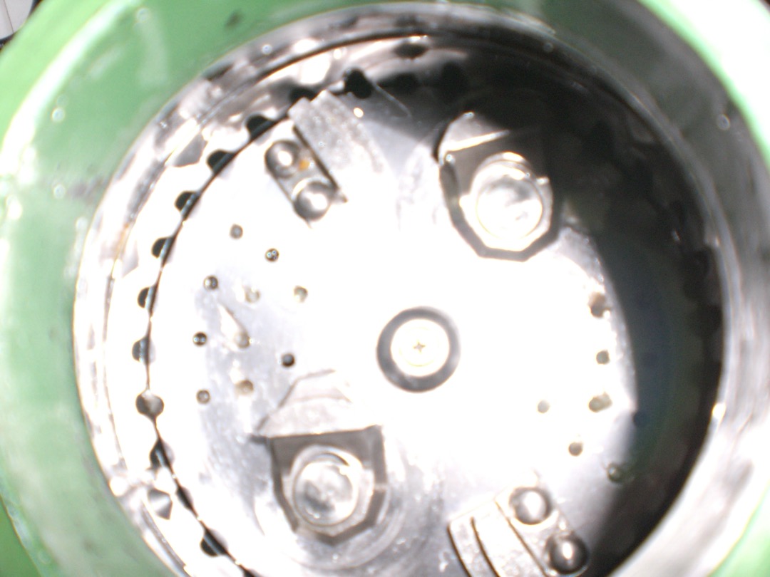 Looking down into a garbage disposal grinding chamber, showing the spinning plate, impeller lugs and serrated grind ring