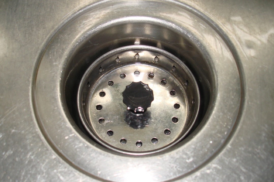 A stainless steel kitchen sink drain photographed from above with water draining cleanly, illustrating a properly functioning drain after the methods covered in this guide