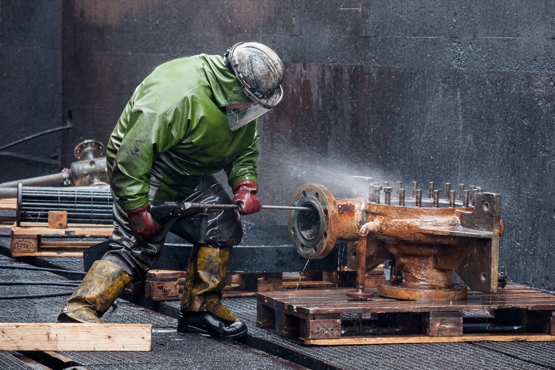 Person using a pressure washer with a fan-spray nozzle to clean an exterior surface