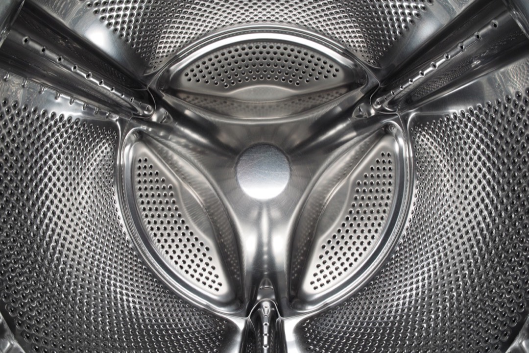 Close-up of the stainless steel interior drum of a washing machine, showing the perforated tub and lifter paddles that this maintenance guide keeps clean and running smoothly